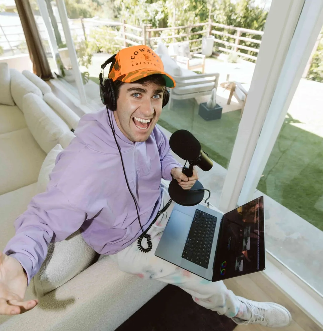 Airrack in a lavender hoodie, holding a microphone with a laptop on his lap